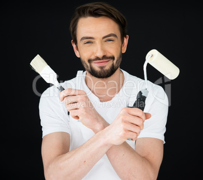 Smiling painter holding a roller and brush