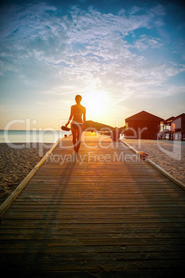 Silhouette of a girl walking along the pier at sunset