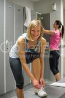 smiling woman tying shoelaces in locker room