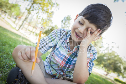 Frustrated Cute Young Boy Holding Pencil Sitting on the Grass