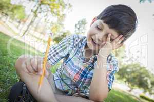 Frustrated Cute Young Boy Holding Pencil Sitting on the Grass
