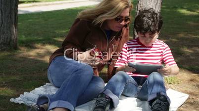mother and son using digital tablet in park