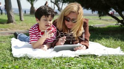 mother and son using digital tablet in park