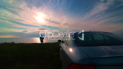 Woman near his car on the sea coast at sunset