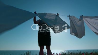 Housewife hanging white sheets on clothesline