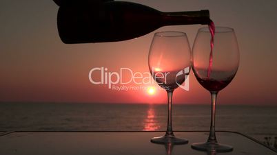 Pouring red wine in two glasses at sunset near the sea