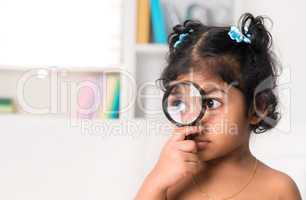 cute indian girl peeking through magnifying glass.