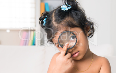 indian girl peers at the camera through a magnifying glass