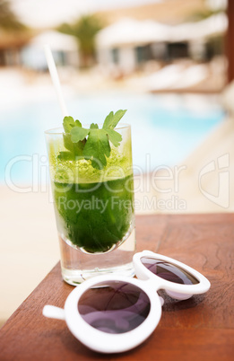 Sunglass and tasty detox cocktail next to swimming pool