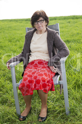 Woman sitting with chair alone in the meadow