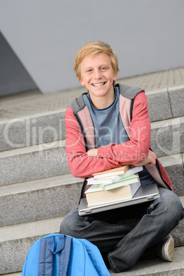 Happy student sitting with books and laptop