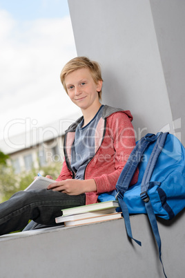 Smiling boy studying sitting on school wall