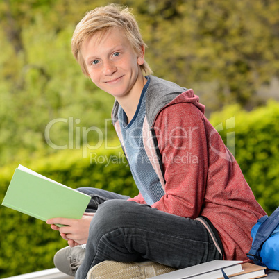 Student boy holding book sitting outside school