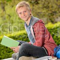 Student boy holding book sitting outside school