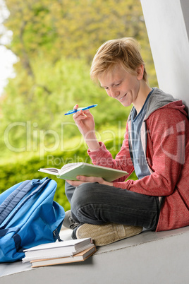 Smiling boy reading book sitting outside school