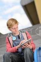 Student boy using tablet sitting on steps