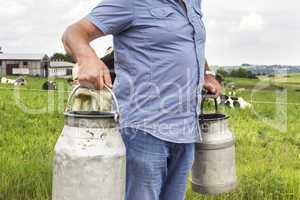 Farmer with milk churns in front of his cows
