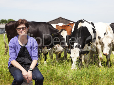 Woman sitting on milk jug in front of the cows