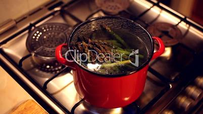 A bunch of asparagus boiling in a red steel bowl full of water