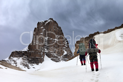 Two hikers in snowy mountains and storm sky