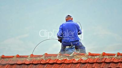 Chimney sweep cleaning a chimney sitting balanced on the apex of a house roof lowering equipment down the flue