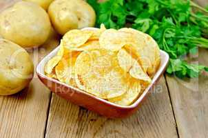 Chips in clay bowl with potatoes on board