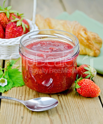 Jam of strawberry with bun and spoon on board