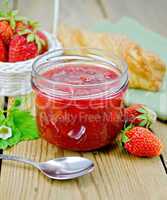 Jam of strawberry with bun and spoon on board