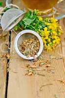 Herbal tea from tutsan in strainer with cup on board