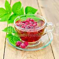 Tea with raspberries in glass cup on board