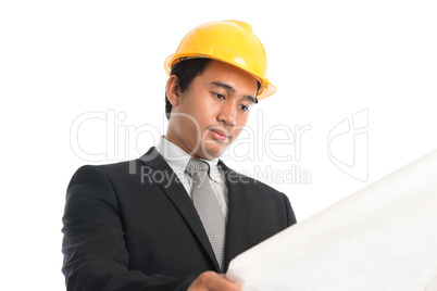 Asian male wearing yellow hardhat looking blue print paper.
