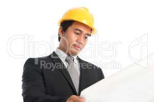 Asian male wearing yellow hardhat looking blue print paper.