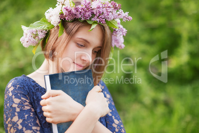 A young girl in a wreath of lilac with a book in hand