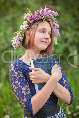 A young girl in a wreath of lilac with a book in hand