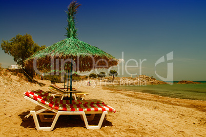 Green straw beach umbrella with sun beds on a beautiful beach
