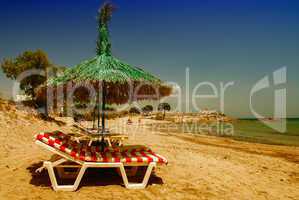 Green straw beach umbrella with sun beds on a beautiful beach