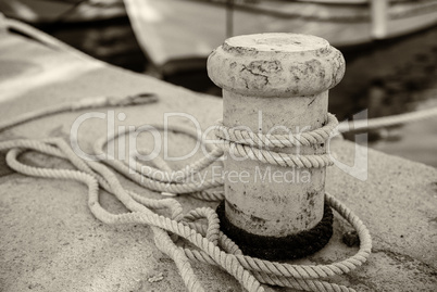 Metal bollard with rope on boat dock and sea