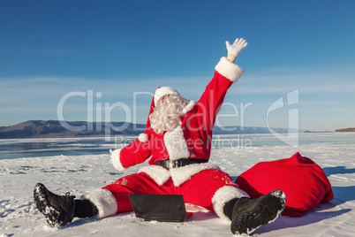 Santa Claus sitting on snow glad news in the laptop
