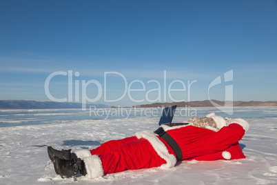 Santa Claus lying on the snow, looking at laptop news