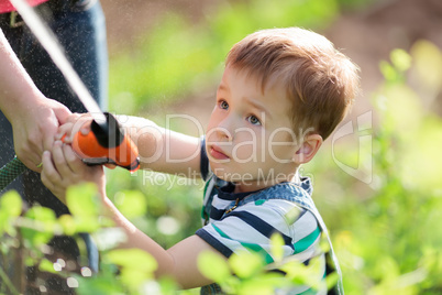Little boy playing with a jet of water in a garden