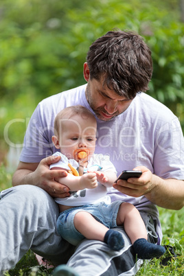 Father using a mobile with a baby on his lap