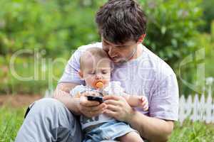 Father holding a baby and texting on his mobile