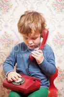 Small boy talking on a red telephone