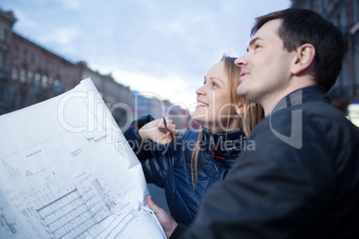 Couple holding blueprints admiring building