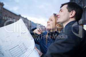 Couple holding blueprints admiring building