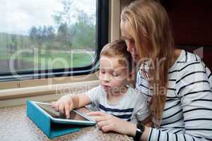 Son and his mom with tablet PC in the train