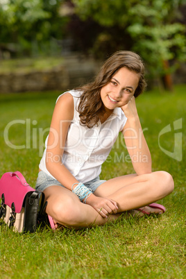 Smiling teenage girl sitting grass with satchel