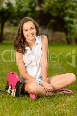 Cheerful student girl with briefcase sitting grass