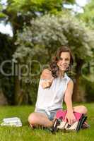 Cheerful student girl sitting grass thumb up