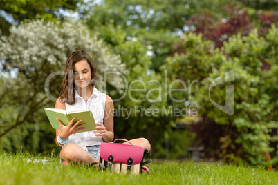 Teenage girl reading book sitting in park